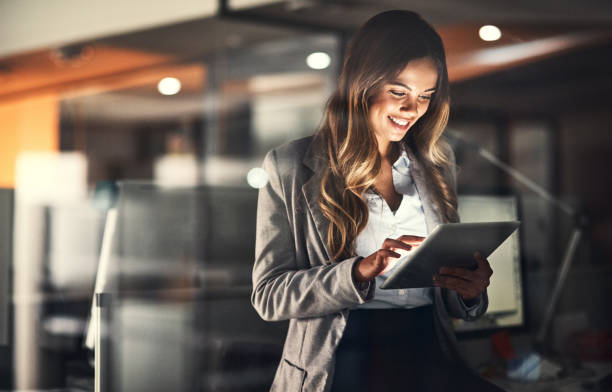 Cropped shot of a young attractive businesswoman using a tablet while working late at night in the office